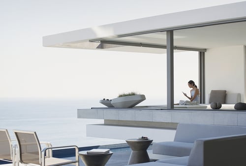 Modern seaside patio with minimalist furniture overlooking the ocean. A person relaxes, reading and conveying a calm, peaceful atmosphere.