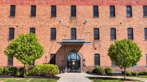 A red brick building with a large arched entrance and two trees in front.at Riverpoint Lofts, Des Moines, IA