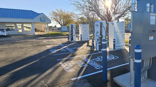 Several EVgo fast-charging units installed in marked parking spaces at a public charging station, with EVgo logos on the chargers, protective bollards around each unit