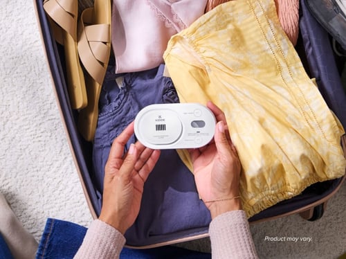 A person holds a CO alarm above a suitcase full of clothes.