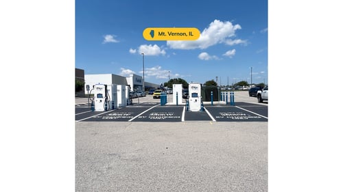 Several EVgo fast charging units installed in marked parking spaces at a public charging station, with EVgo logos on the chargers, protective bollards around each unit. CCS chargers featured in the image.