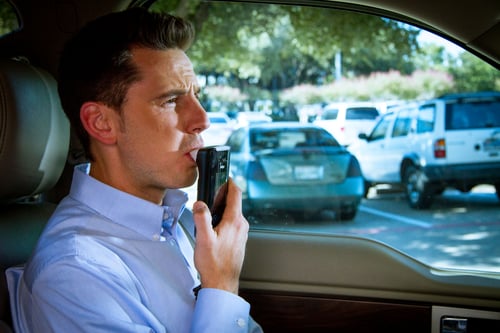 Man blowing into Draeger Interlock 7000 ignition interlock device inside a parked vehicle.
