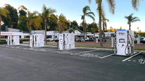 Several EVgo fast-charging units installed in marked parking spaces at a public charging station, with EVgo logos on the chargers, protective bollards around each unit