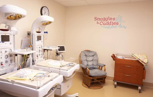 A view of the nursery showing a rocker recliner, bassinet and infant warmers.