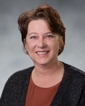 Kim Benning, APRN, CNP smiling in front of a gray background.