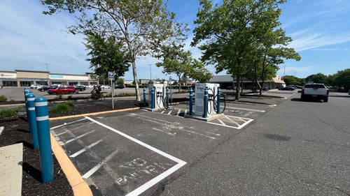 Several EVgo fast charging units installed in marked parking spaces at a public charging station, with EVgo logos on the chargers, protective bollards around each unit