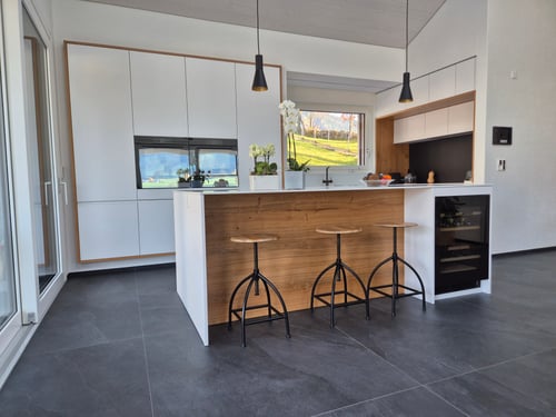 Cuisine aux volumes épurés, où les façades blanches mates se marient harmonieusement avec des accents de bois naturel et des détails noirs.