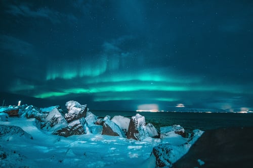 Picture of the northern lights shining above a body of water with a snowy shore.