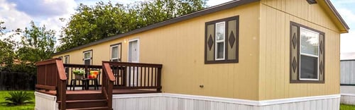 a yellow house with a wooden deck and a tree in the background at Regency Village in San Antonio, TX