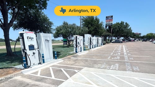 Several EVgo fast charging units installed in marked parking spaces at a public charging station, with EVgo logos on the chargers, protective bollards around each unit.
