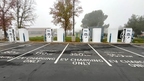 Several EVgo fast-charging units installed in marked parking spaces at a public charging station, with EVgo logos on the chargers, protective bollards around each unit