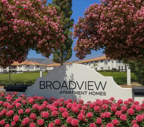 A sign for Broadview Apartment Homes is surrounded by pink flowers.