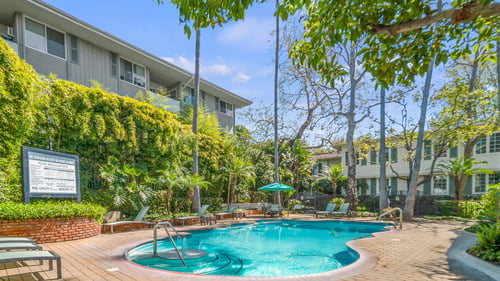 A pool surrounded by a wooden deck and green trees at Sunset Barrington Gardens, Los Angeles, 90049