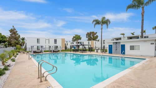 A swimming pool surrounded by palm trees and buildings at Tamarack Sands Apartment Homes