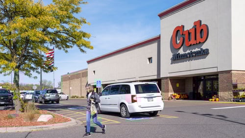 Person walking past white van with tree in front at entrance of Cub grocery store at Westwind Plaza shopping center