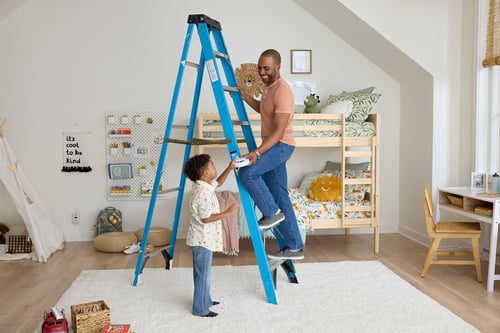 A dad accepts a smoke alarm from his son as he climbs a ladder.