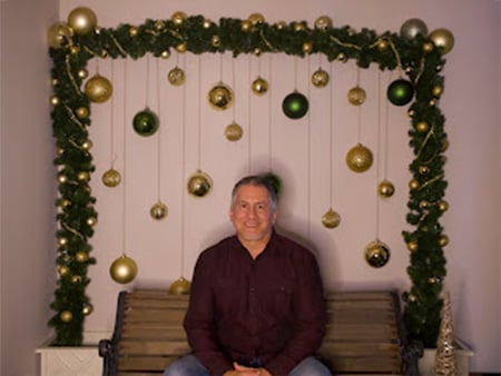 Al, a chiropractic assistant at the Hurst location of Absolute Chiropractic & Rehab sitting on a bench in front of office Christmas decorations