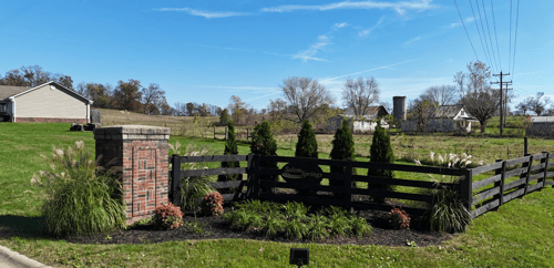 Salem Springs community entrance sign displayed on a black wooden fence with manicured landscaping, brick column, and a rural countryside backdrop under a bright blue sky.