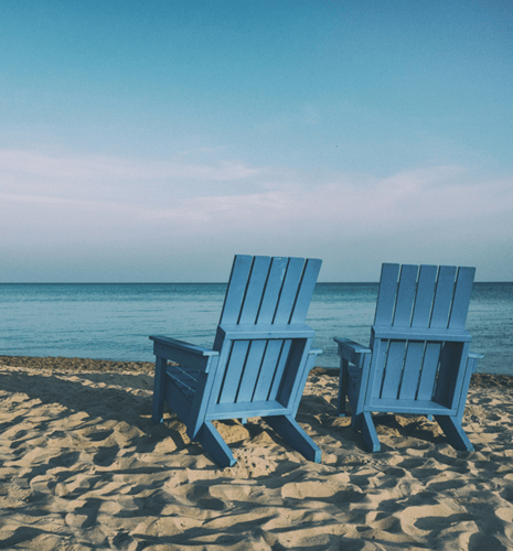 Two blue wooden beach chairs placed on a sandy beach