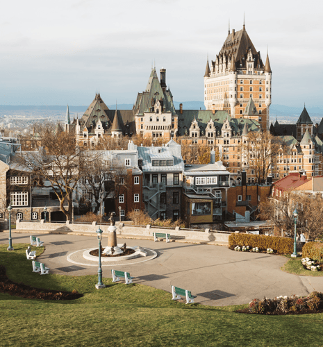 Historic buildings with green roofs and a castle-like tower dominate the skyline, framed by a scenic park with benches and flowerbeds.