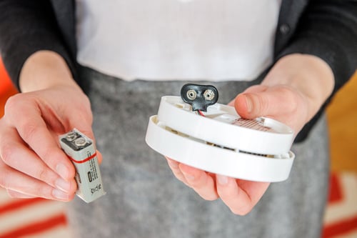 An individual installing a 9V battery into a smoke detector to ensure home safety.