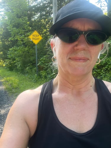 Selfie of Colleen on a Sunny day,  A yellow "NO EXIT" road sign behind her.