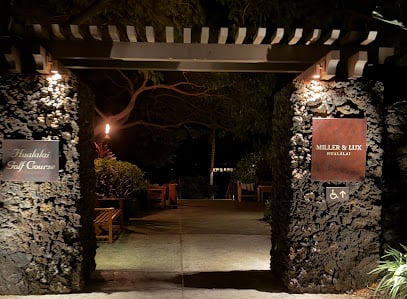 Tropical restaurant with stone walls, wooden balconies and an open-air dining area, surrounded by lush greenery and palm trees