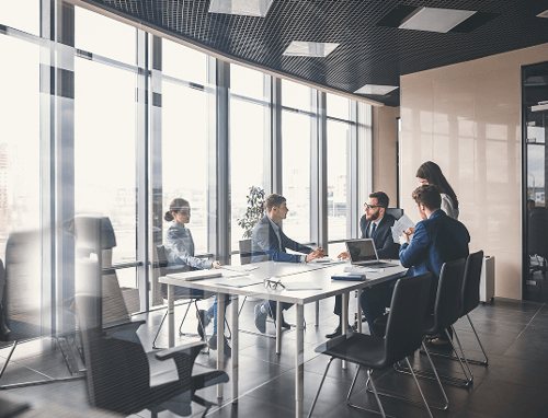 A group of professionals having a meeting in a modern, bright office with large windows.