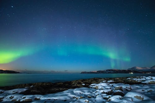 Picture of the northern lights shining above a body of water with a snowy shore.