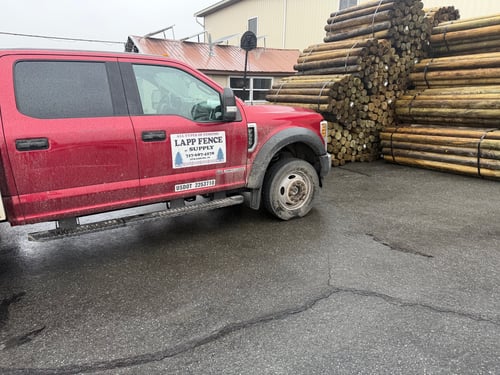 Red truck with Lapp Fence Supply Logo parked in front of stacks of fencing supplies.