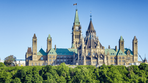 Ottawa's Parliament Hill under a clear blue sky, featuring the iconic Gothic-style buildings with green roofs and the Canadian flag atop the Peace Tower.