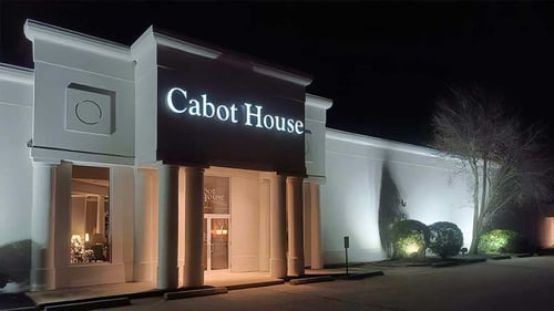 Storefront of Cabot House Furniture Waymouth location at night with lit up entryway and landscaping.