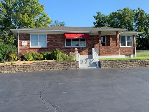 Brick building with green grass and bushes and red awning