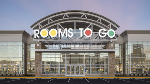 Exterior view of the Rooms To Go furniture store in Buford, GA, near the Mall of Georgia, showcasing a modern facade with large glass windows and the iconic Rooms To Go signage.