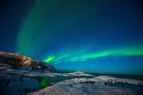 Picture of the northern lights shining above a body of water with a snowy shore.