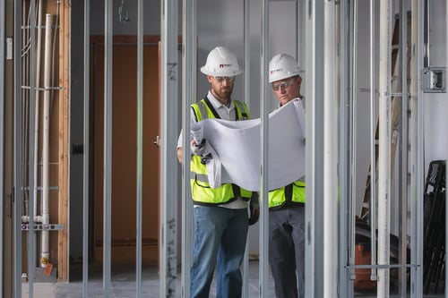 Photo of Mappco Construction managers analyzing blueprints on a construction site with exposed metal stud framing, exemplifying their detail-oriented project management and expertise in commercial building.