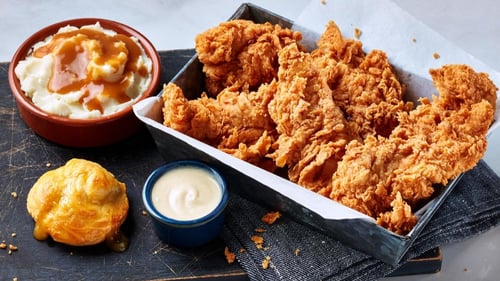 A serving tray displaying golden fried, hand-breaded chicken jumbo tenders with a side of fluffy mashed potatoes and savory gravy.