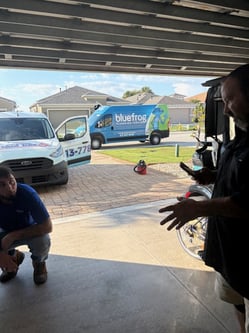 bluefrog plumber kneeling in a garage with a professional restoration technician