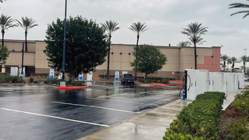 Several EVgo fast-charging units installed in marked parking spaces at a public charging station, with EVgo logos on the chargers, protective bollards around each unit