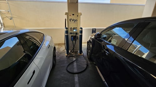 Several EVgo fast charging units installed in marked parking spaces at a public charging station, with EVgo logos on the chargers, protective bollards around each unit.