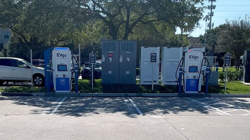Several EVgo fast-charging units installed in marked parking spaces at a public charging station, with EVgo logos on the chargers, protective bollards around each unit