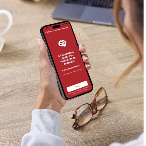 Une femme regarde son smartphone, qui affiche une alerte de détection de monoxyde de carbone.