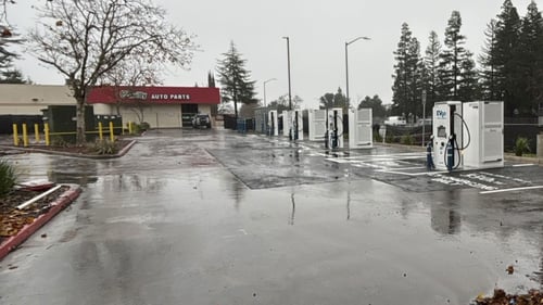 Several EVgo fast-charging units installed in marked parking spaces at a public charging station, with EVgo logos on the chargers, protective bollards around each unit