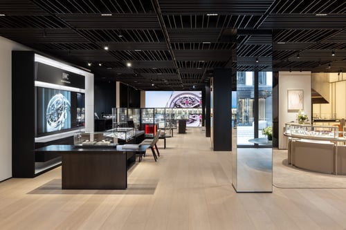 Modern watch showroom with IWC display wall and glass cases.