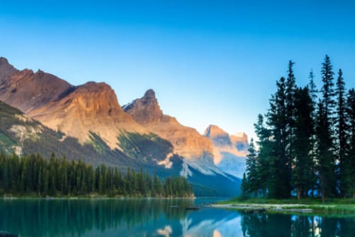 Picturesque alpine landscape featuring a calm lake reflecting the surrounding trees and mountains.