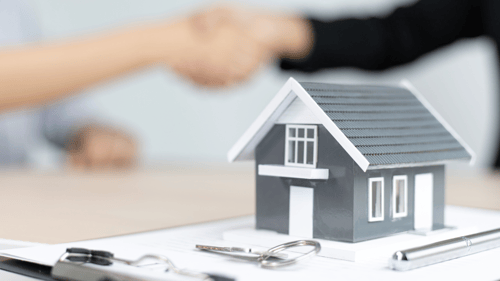 real estate agent and buyer shaking hands behind a model of a house