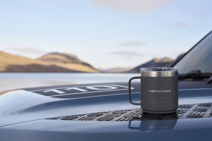 Defender YETI mug placed on the bonnet of a Defender with a mountain lake in the background.