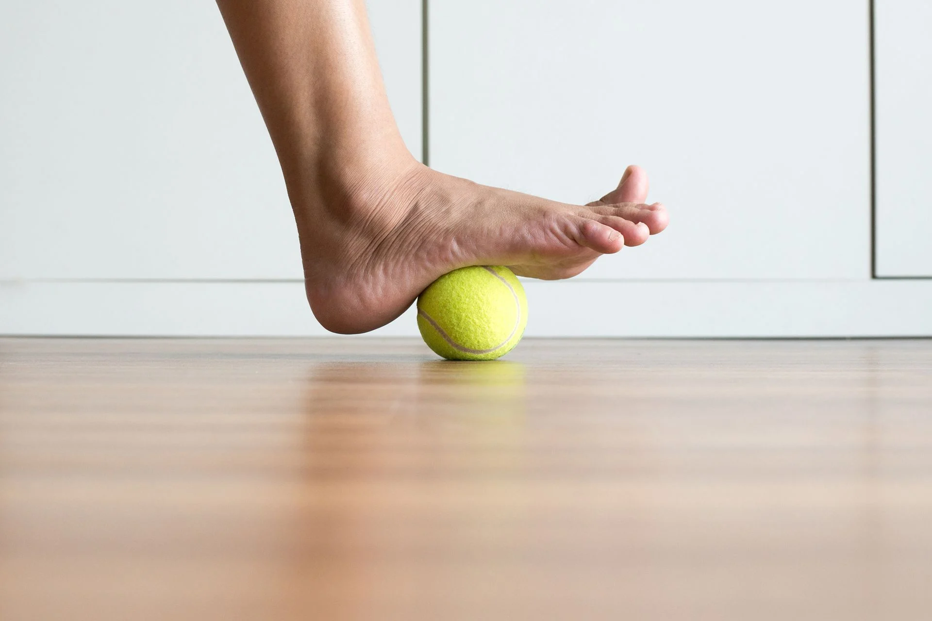 person doing plantar fasciitis stretches by rolling foot on tennis ball