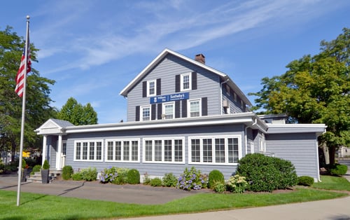 Gray colonial-style building with black shutters and white-trimmed windows housing William Pitt Sotheby's International Realty in Westport, Connecticut, featuring American flag and hydrangea gardens.