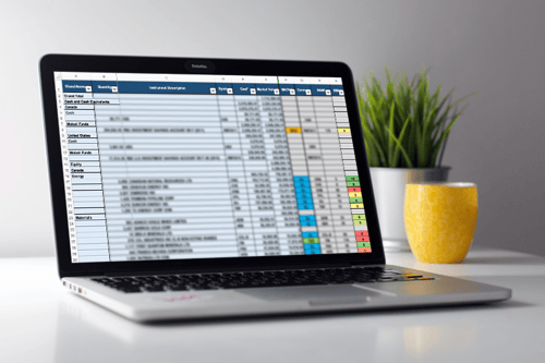 A laptop opened on a desk, showing a spreadsheet on the screen.